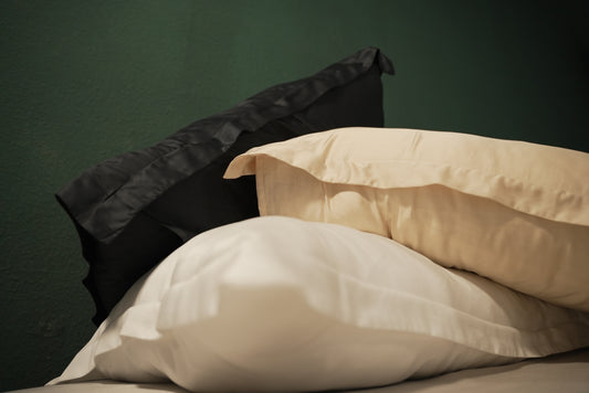 Three pillows, one Raven black, one pearl white and one bubbly champagne, on a bed against a dark green wall.