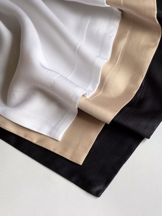 Stack of BetterBe bamboo pillowcases in Raven Black, Pearl White and Bubbly Champagne, smooth weave close up
