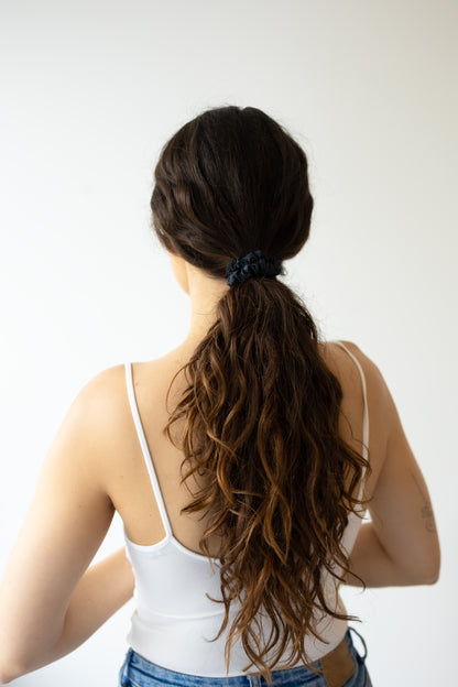 Person with long hair in a ponytail wearing a white tank top against a plain background