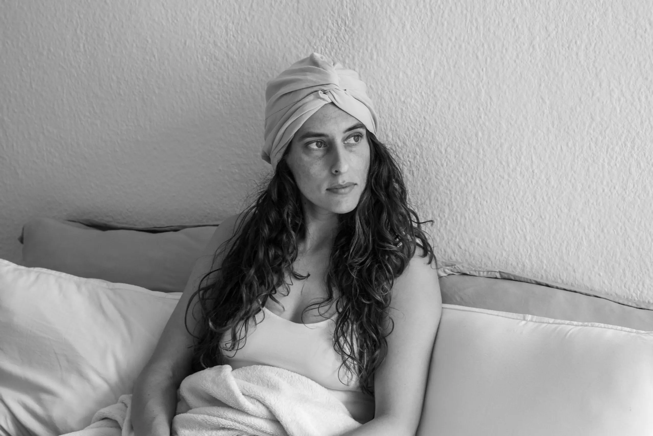 Model with beautiful brown curls lying in bed, wearing a bamboo hair bonnet. The bonnet protects her hair while she sleeps, keeping her curls frizz-free and moisturized.