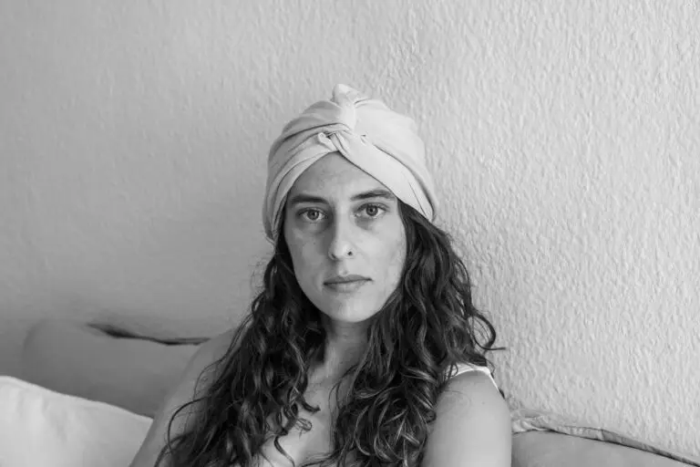 Model with beautiful brown curls resting in bed, wearing a 100% bamboo hair bonnet, an eco-friendly alternative to silk and satin hair bonnets, protecting her curls overnight while reducing frizz and retaining moisture.